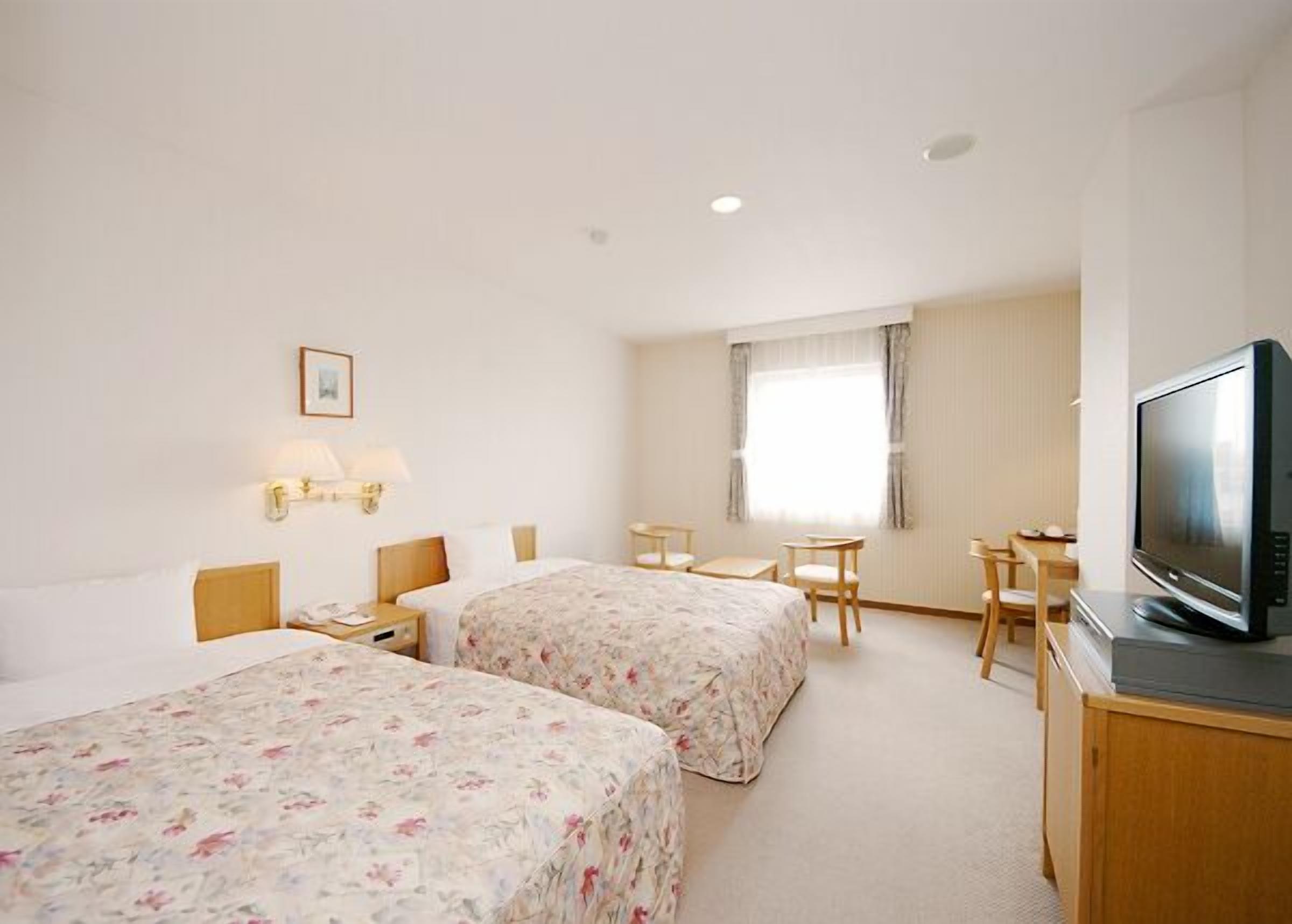 A hotel room with two beds, a television, a desk, and a window.