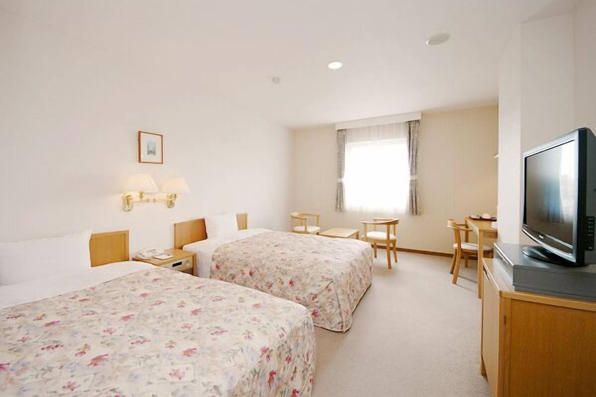 A hotel room with two beds, a television, a desk, and a window.