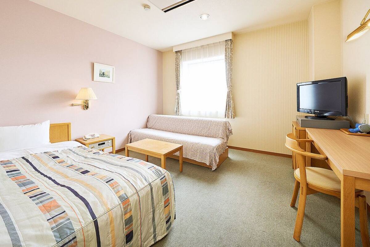 A hotel room with a bed, a desk, a television, a lamp, and a window with curtains.