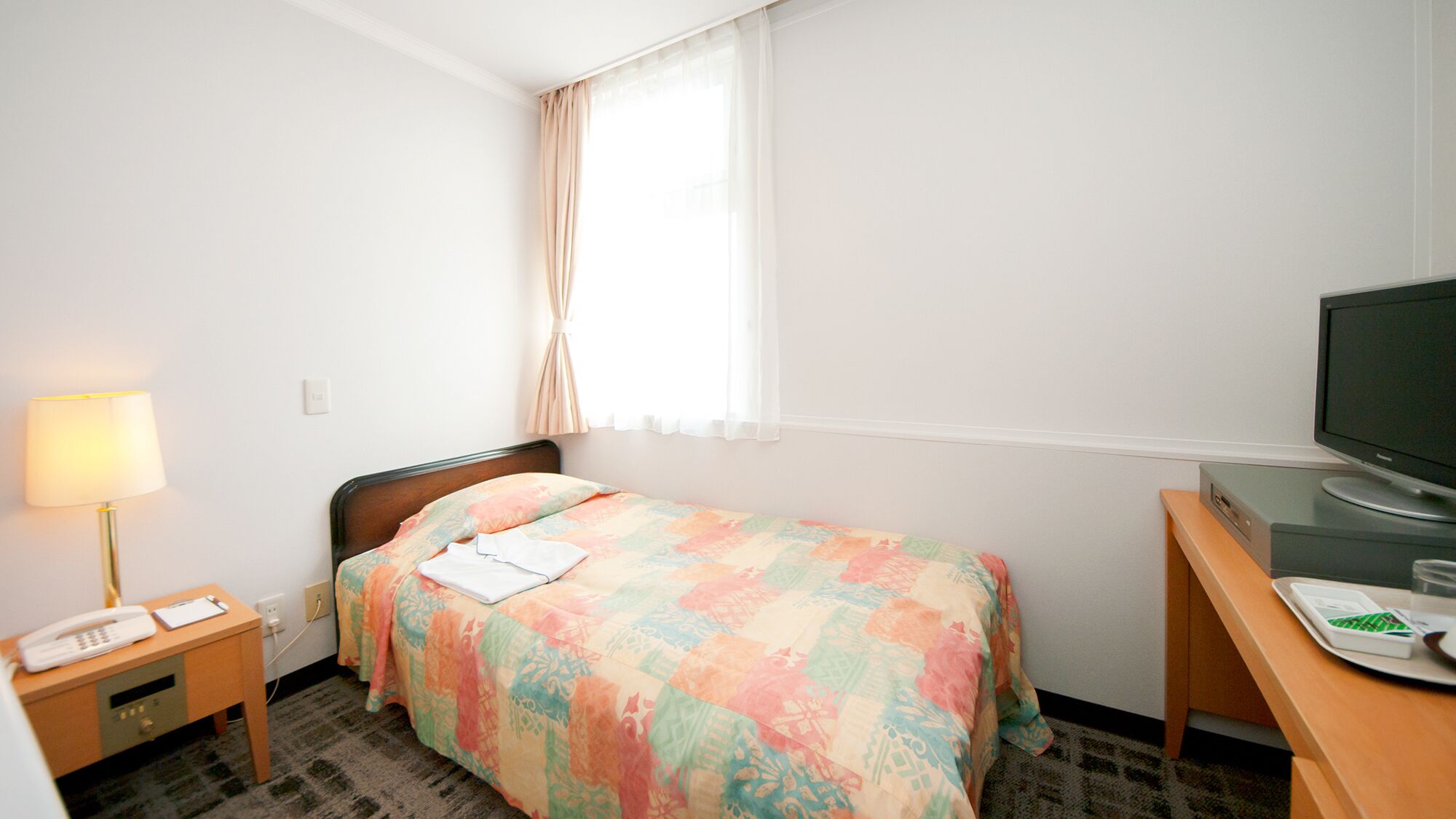 A hotel room with a bed, a desk, a television, a lamp, and a telephone.