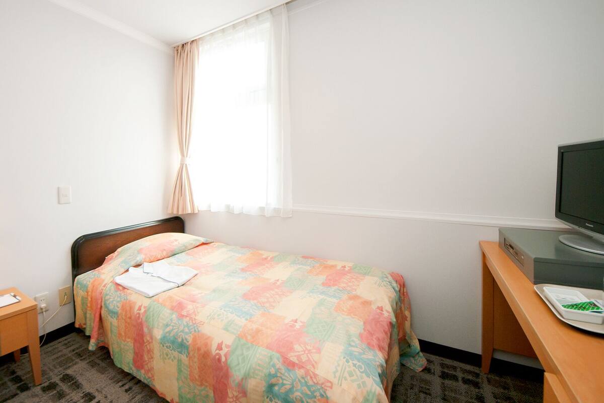 A hotel room with a bed, a desk, a television, a lamp, and a telephone.