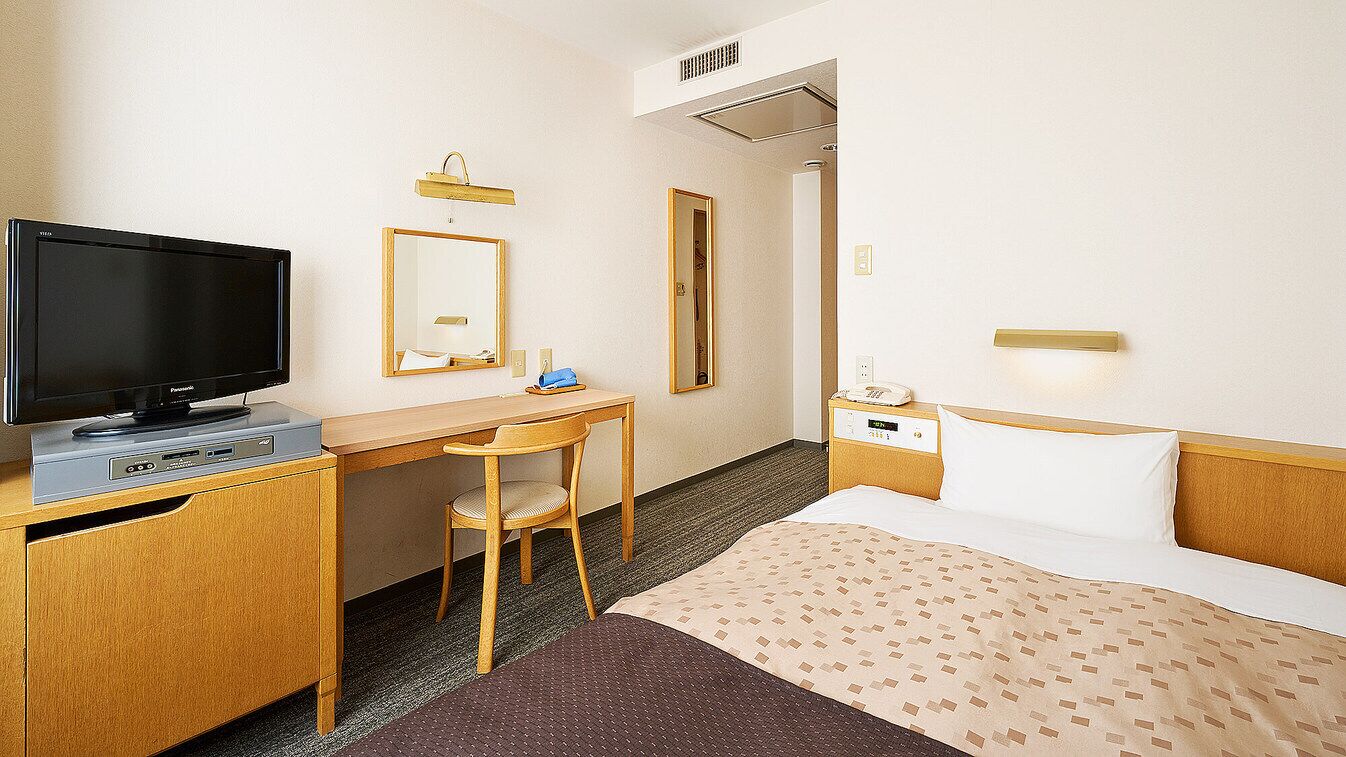 Habitación de hotel con cama, escritorio con televisor, una silla, mesita de noche con teléfono y espejo.
