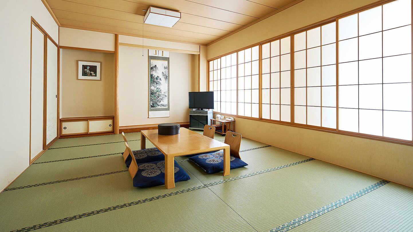 Una habitación japonesa tradicional con suelo de tatami, una mesa baja, un televisor y puertas correderas.