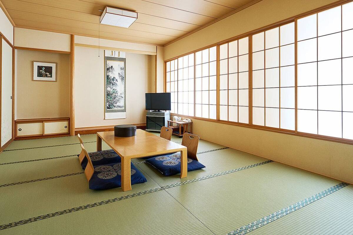 A traditional Japanese room with tatami flooring, a low table, a television, and sliding doors.