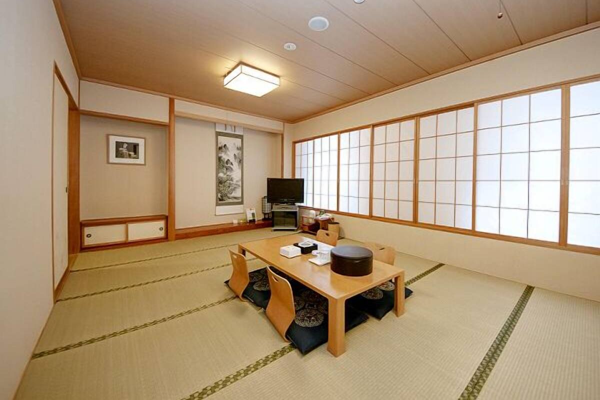 A traditional Japanese room with tatami flooring, a low table, a television, and sliding doors.