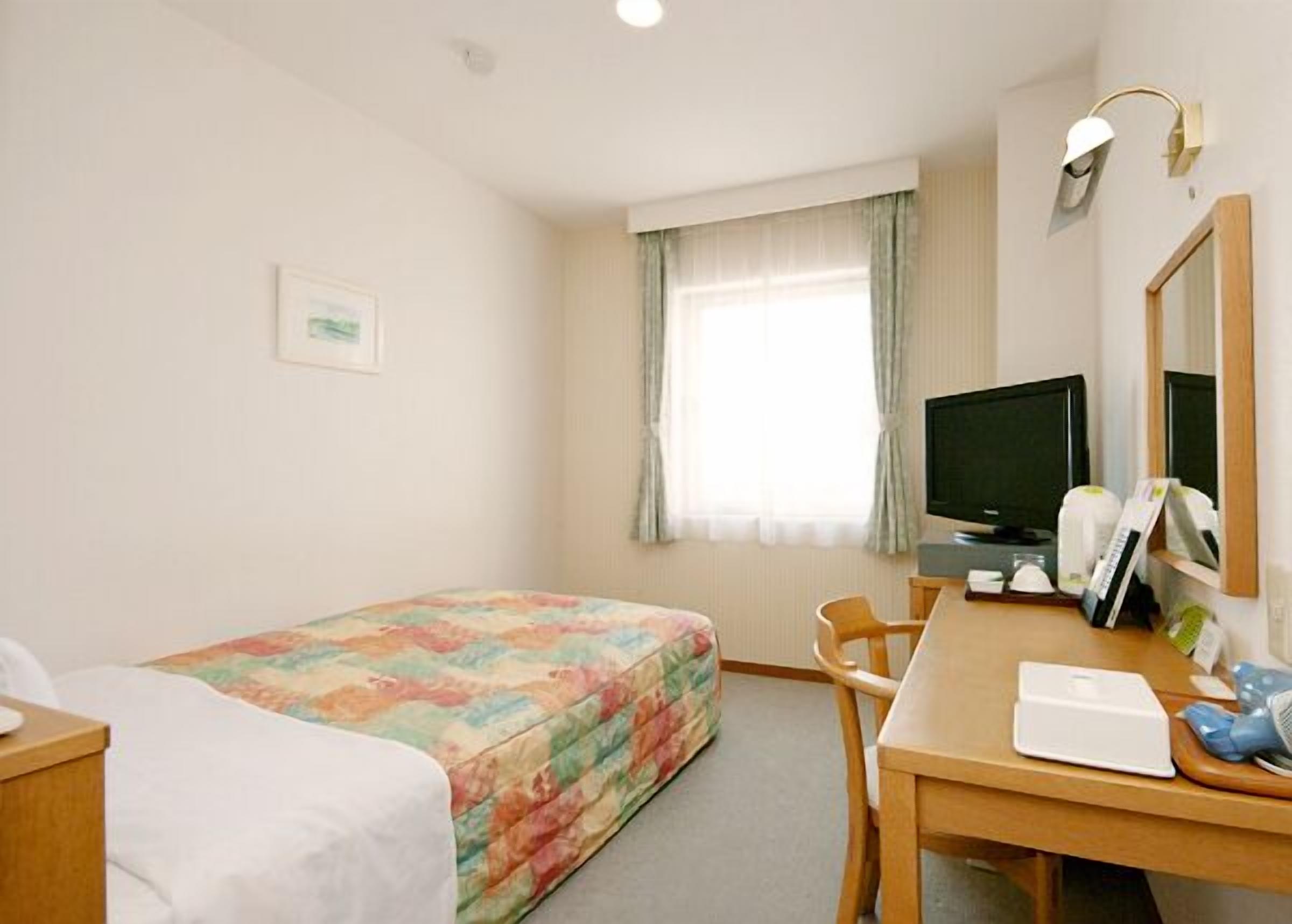 A hotel room with a bed, a desk, a chair, a television, and a window with curtains.