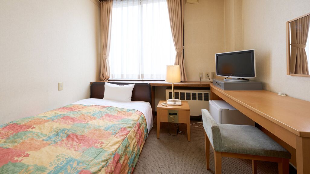 Una habitación de hotel con una cama, un escritorio con un ordenador, una silla y un televisor.