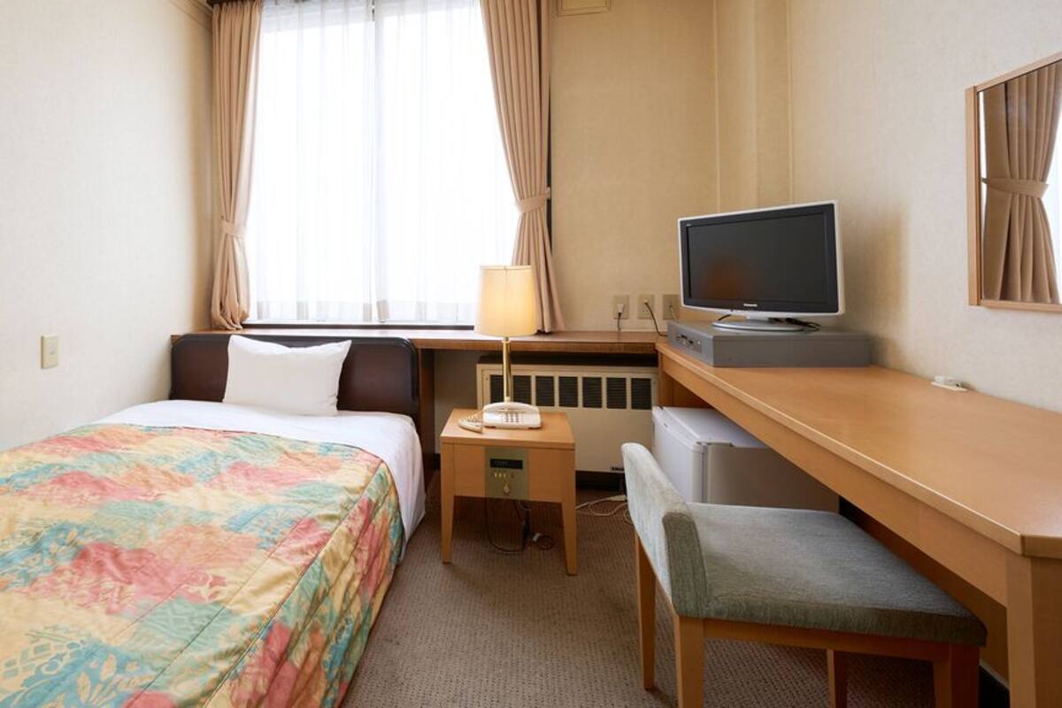 A hotel room with a bed, a desk with a computer, a chair, and a television.