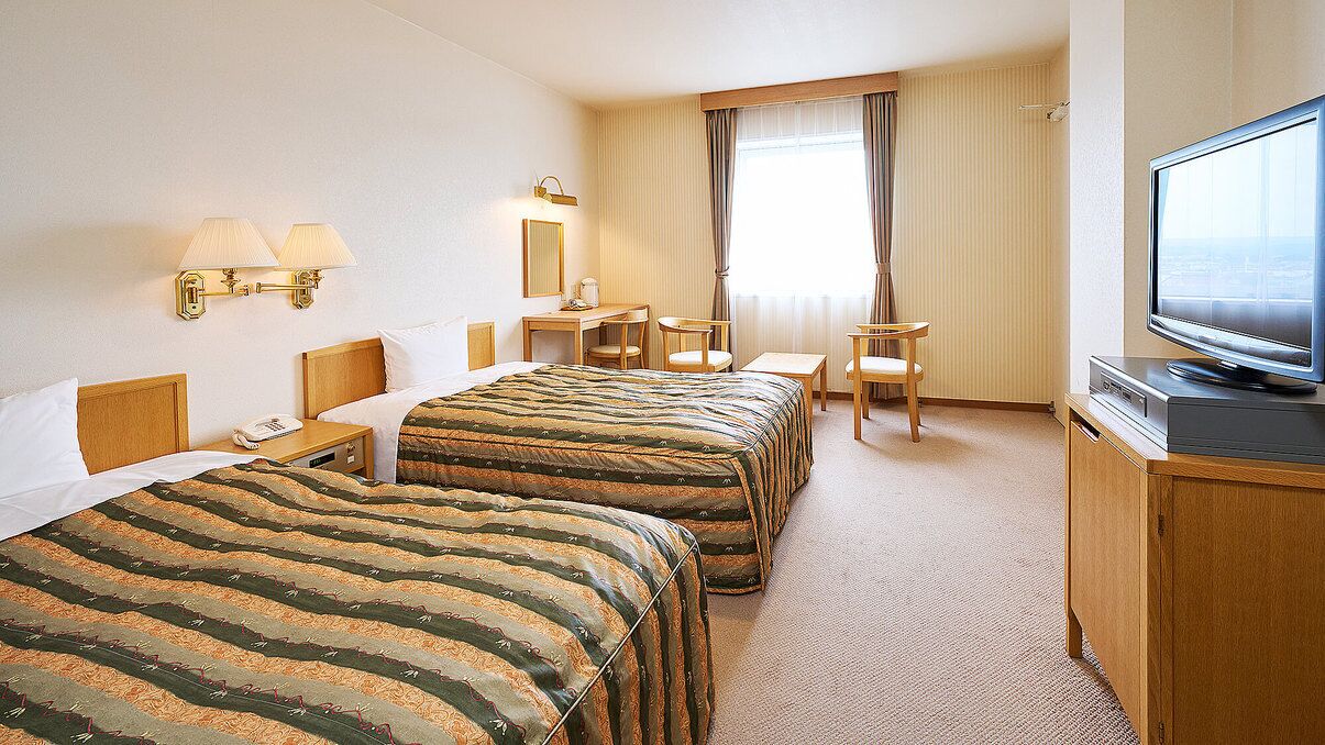 Habitación de hotel con dos camas, un escritorio, una silla, un televisor y una ventana con cortinas.