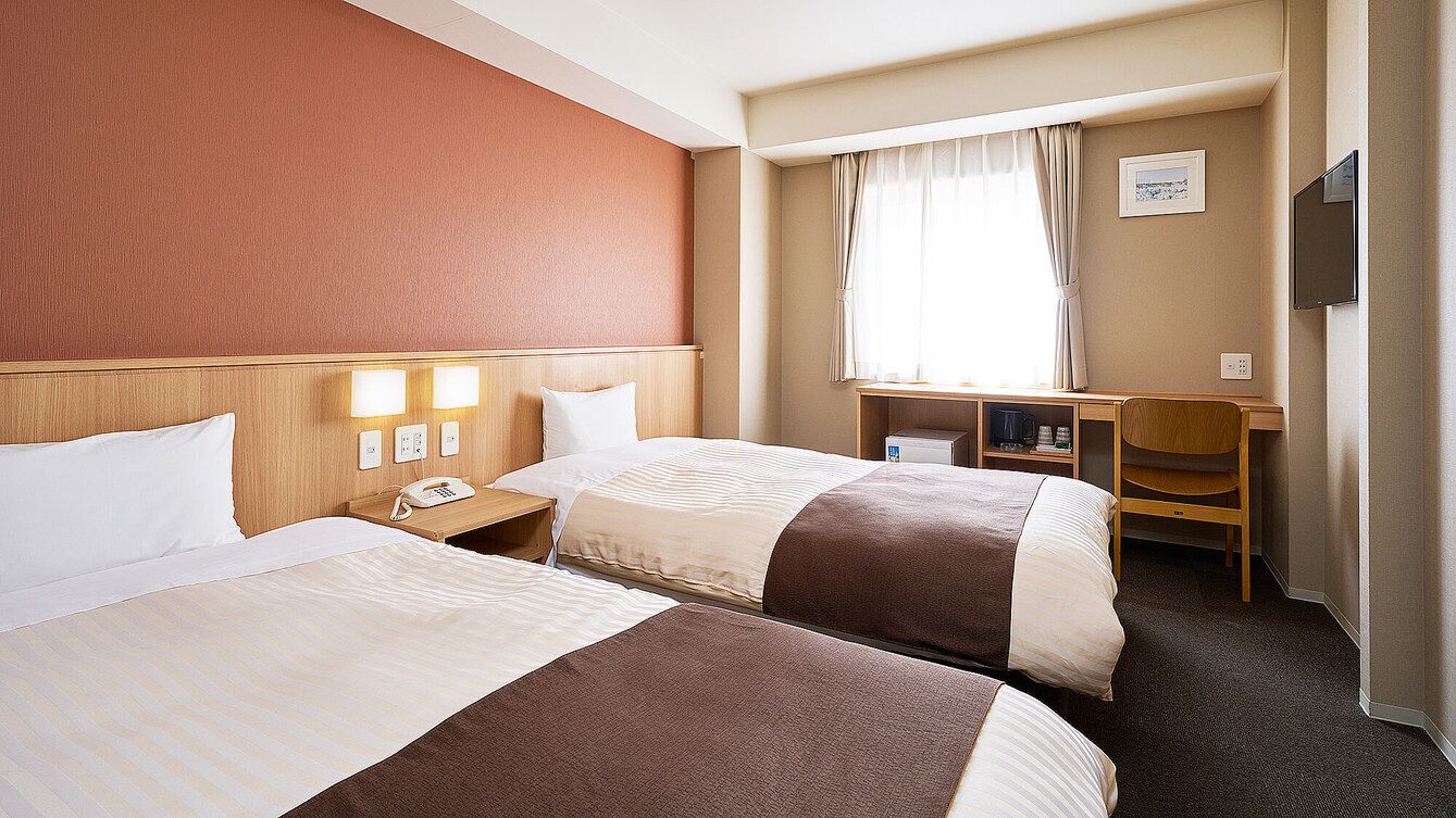 Habitación de hotel con dos camas, un escritorio, una silla, un televisor y una ventana con cortinas.