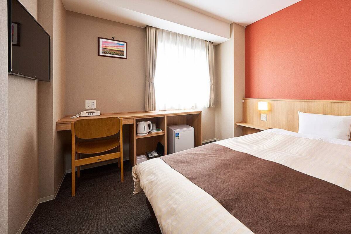 A hotel room with a bed, desk, chair, and a television.