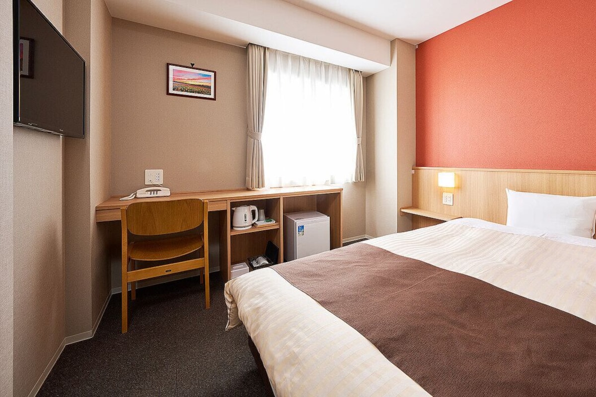 Una habitación de hotel con cama, escritorio, silla y televisor.