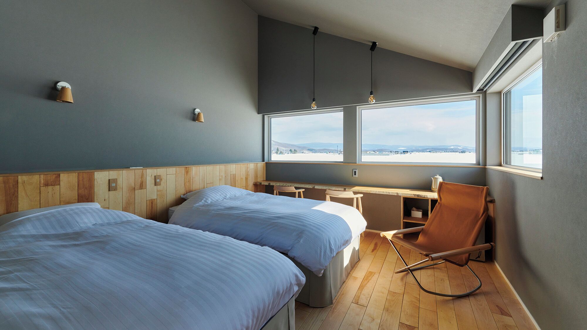 Una habitación con dos camas, un escritorio, una silla y un ventanal con vistas.