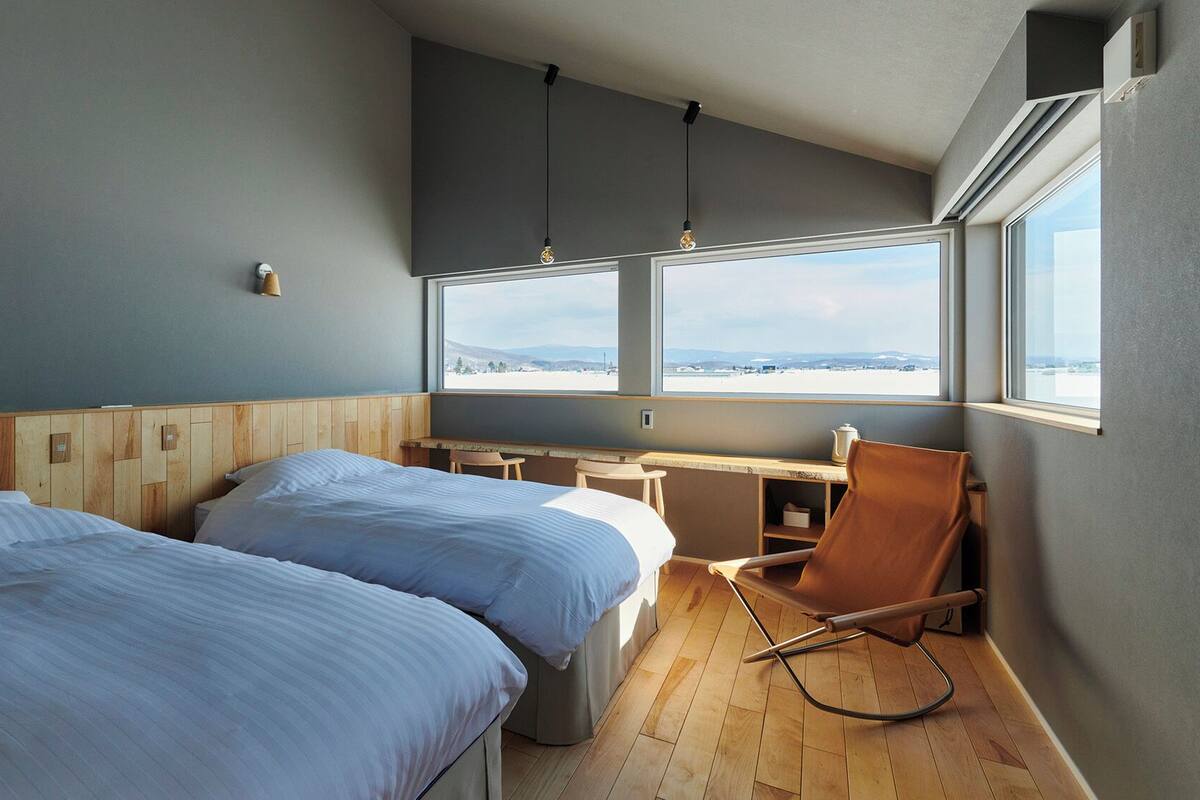Una habitación con dos camas, un escritorio, una silla y un ventanal con vistas.