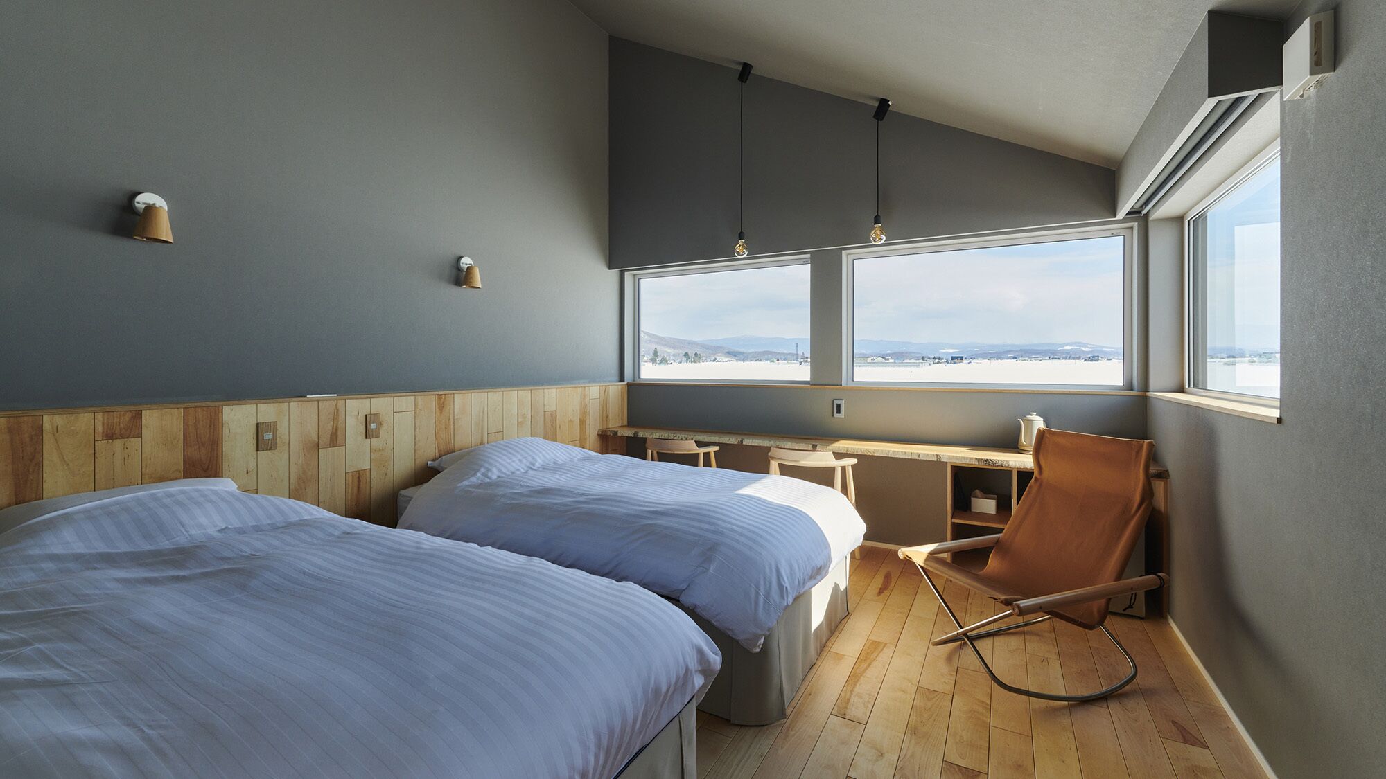 Una habitación con dos camas, un escritorio, una silla y un amplio ventanal con vistas.