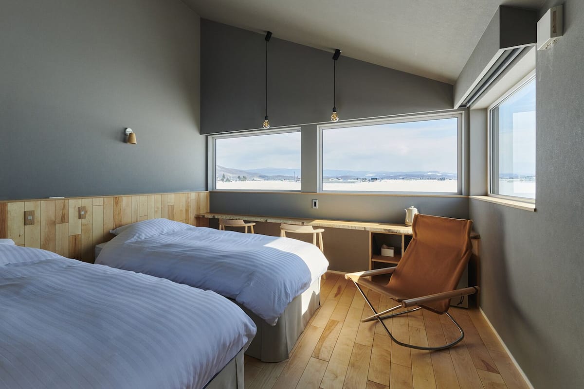 Una habitación con dos camas, un escritorio, una silla y un amplio ventanal con vistas.
