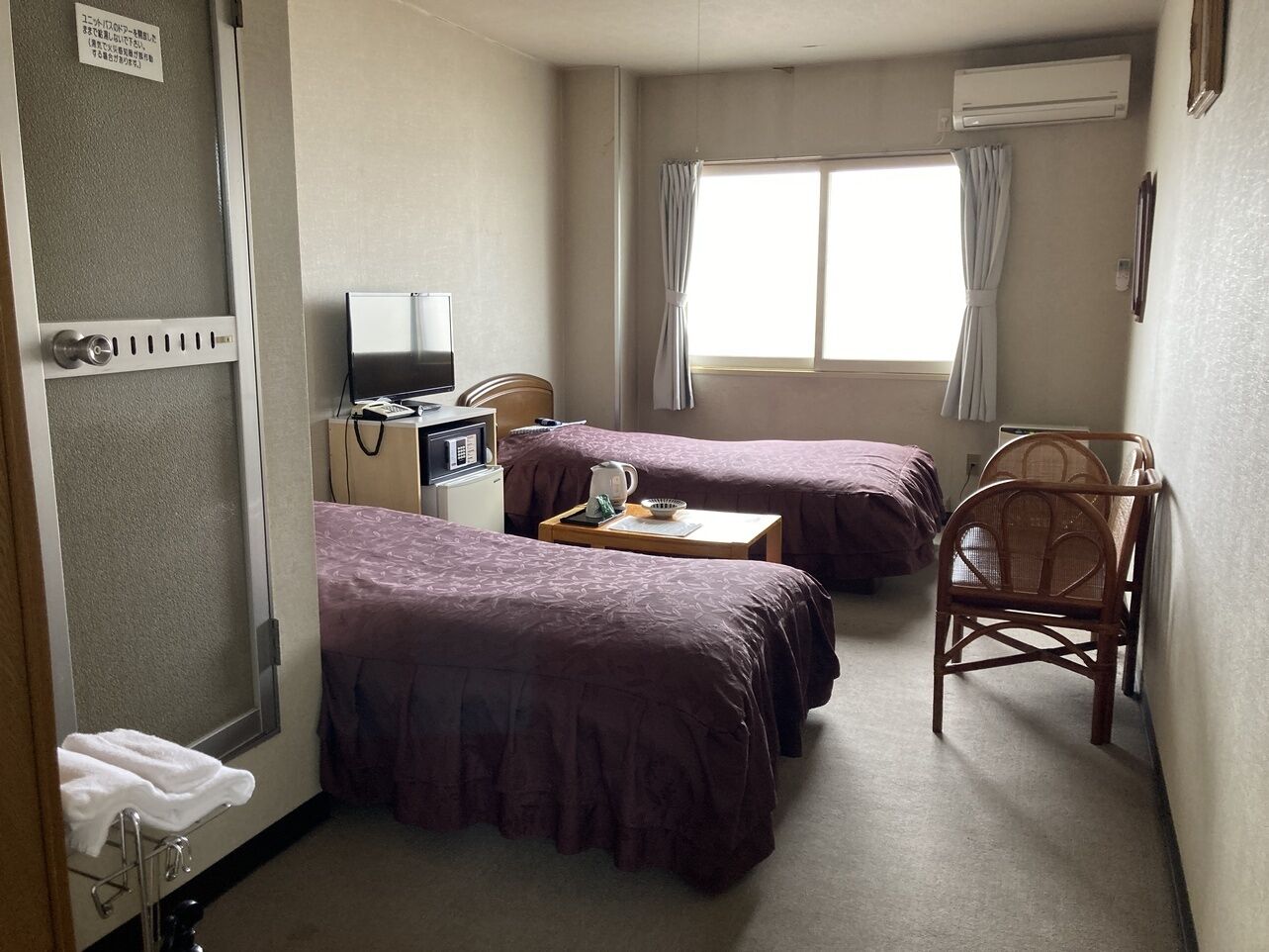 A hotel room with two beds, a desk with a computer, a chair, and a window with curtains.