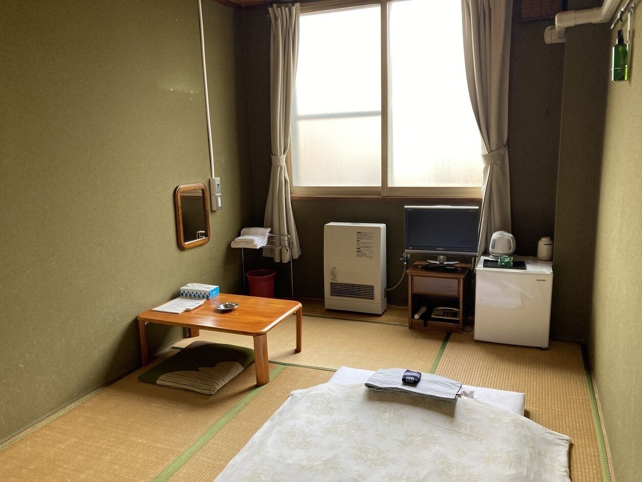 A hotel room with a bed, a small table, a desk, a television, a heater, and a window with curtains.