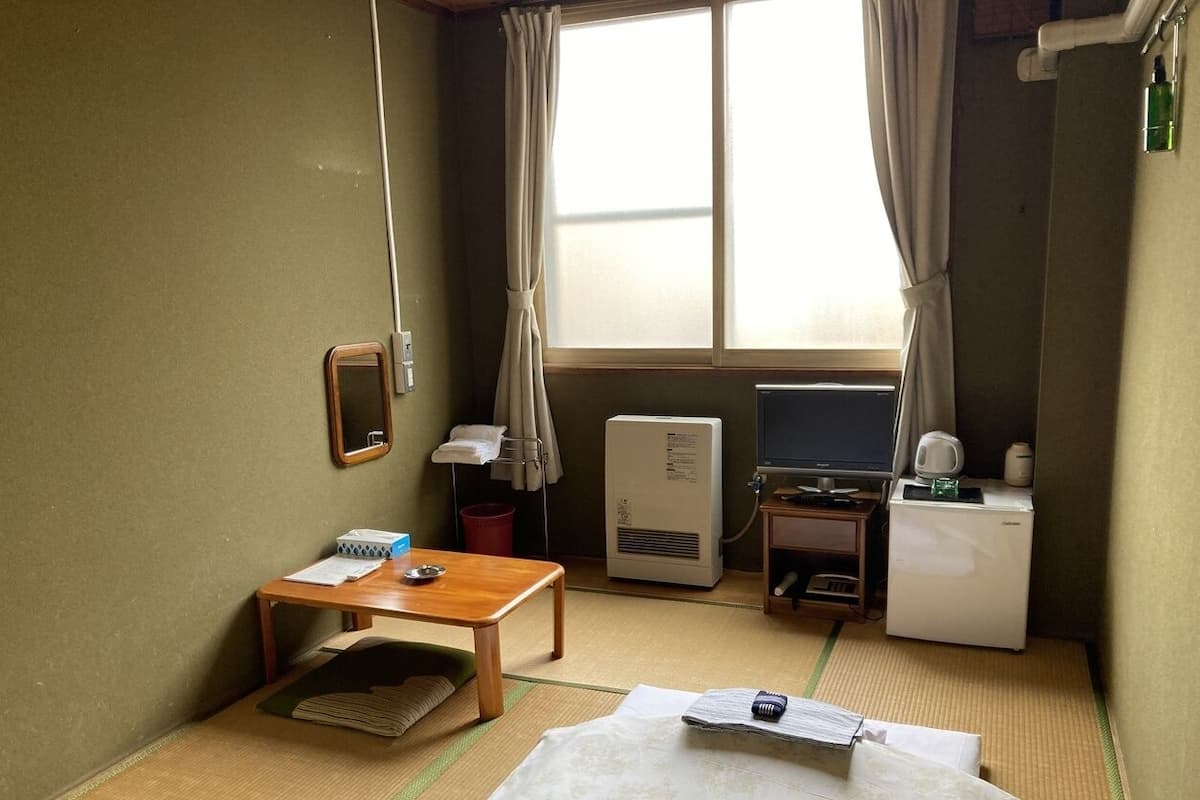 Habitación de hotel con cama, una mesita, escritorio, televisión, calefactor y ventana con cortinas.