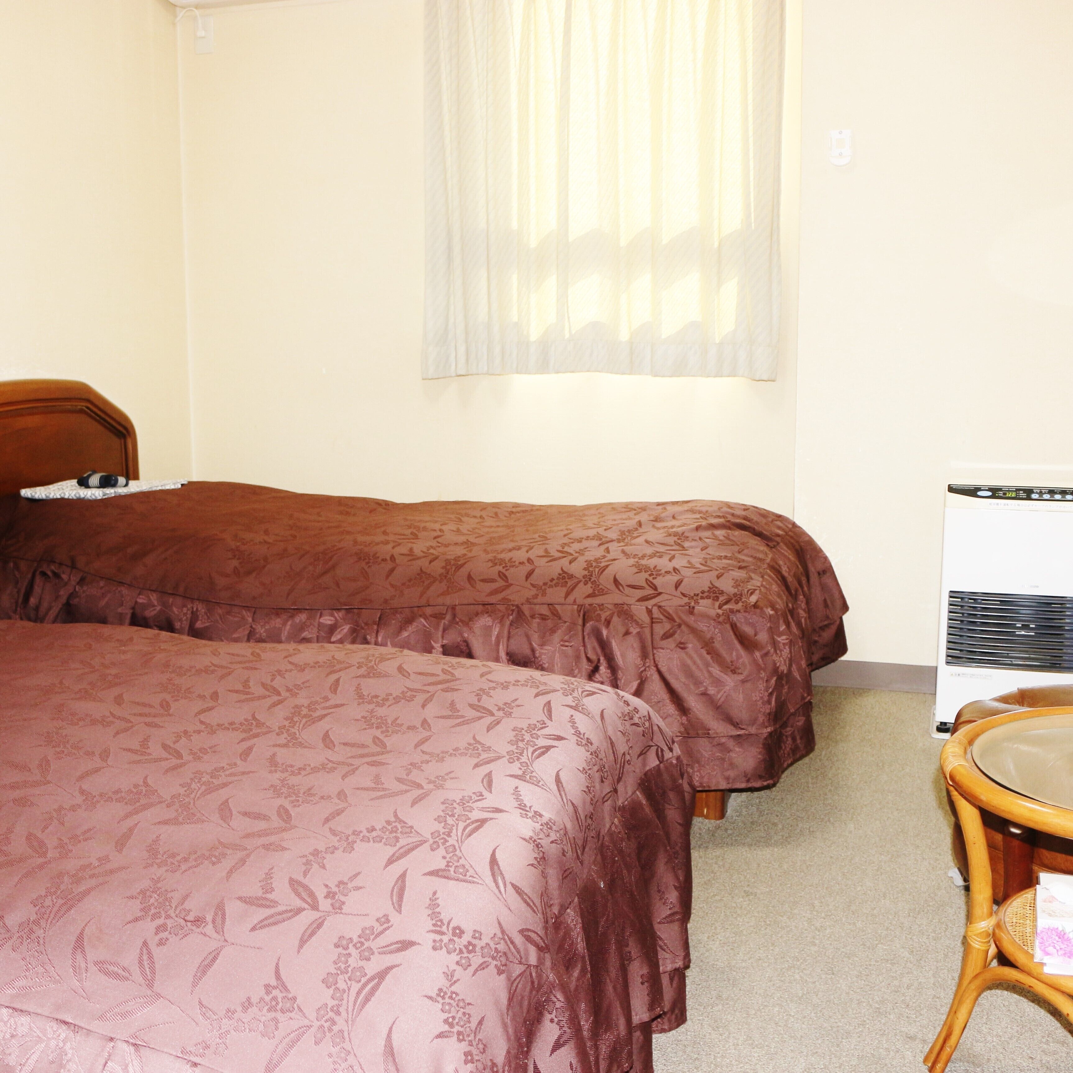 A room with two beds, a chair, a heater, and a window with sheer curtains.