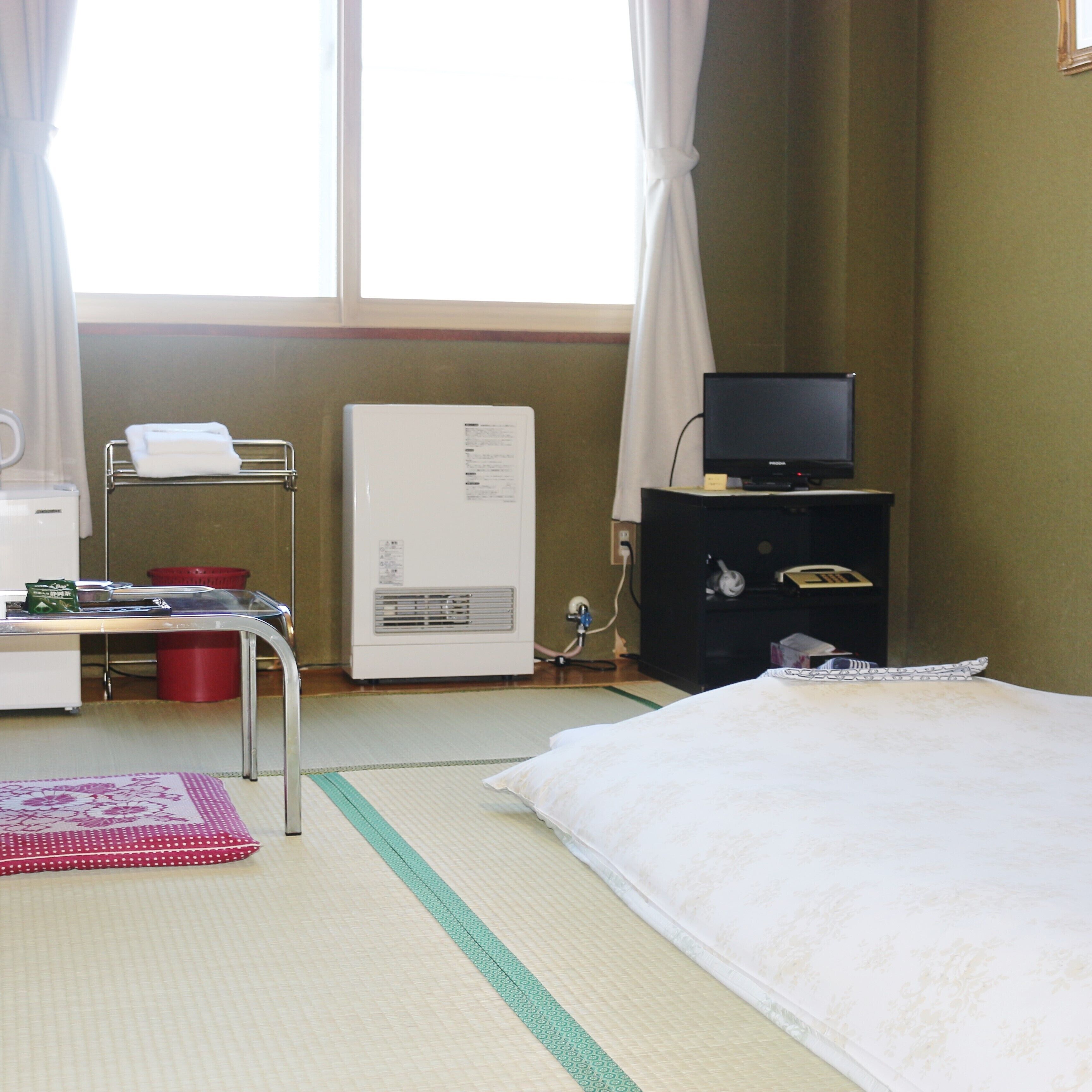 A hotel room with a bed, a desk with a computer, a television on a stand, and a window with curtains.
