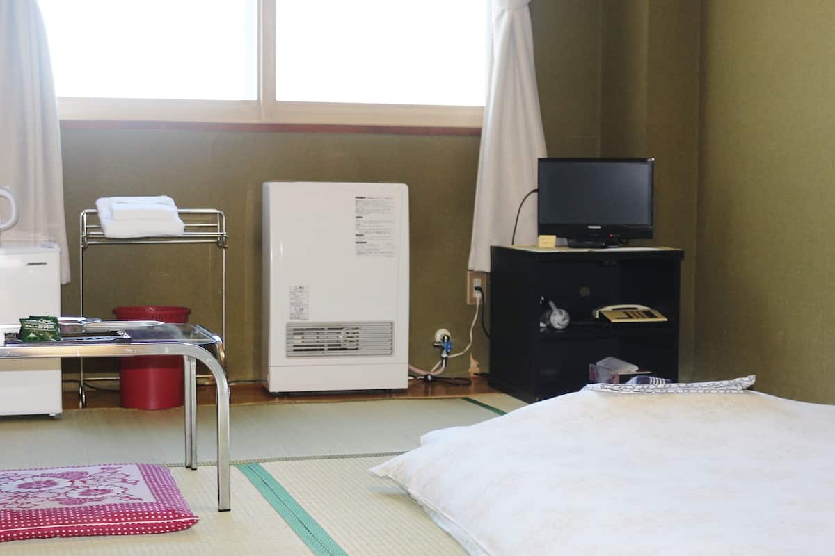 Habitación de hotel con cama, escritorio con computadora, televisor sobre un mueble bajo y ventana con cortinas.