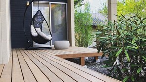 A wooden deck with a hanging chair and a bench, surrounded by greenery. - Morihaku (Karuizawa)