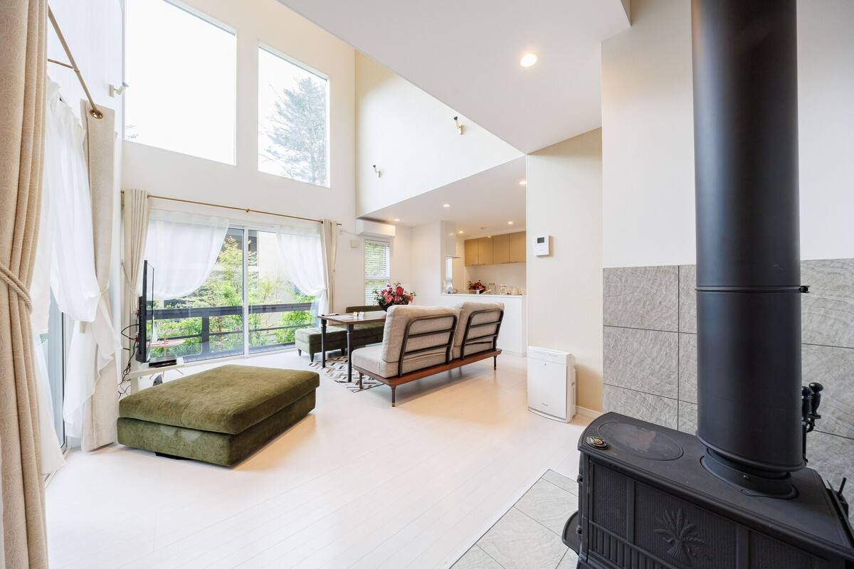 A modern living room with a sofa, a dining area, a kitchen, and a large black stove.