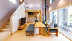 A modern interior with a staircase, a dining area, a sofa set, and a television. - Morihaku (Karuizawa)