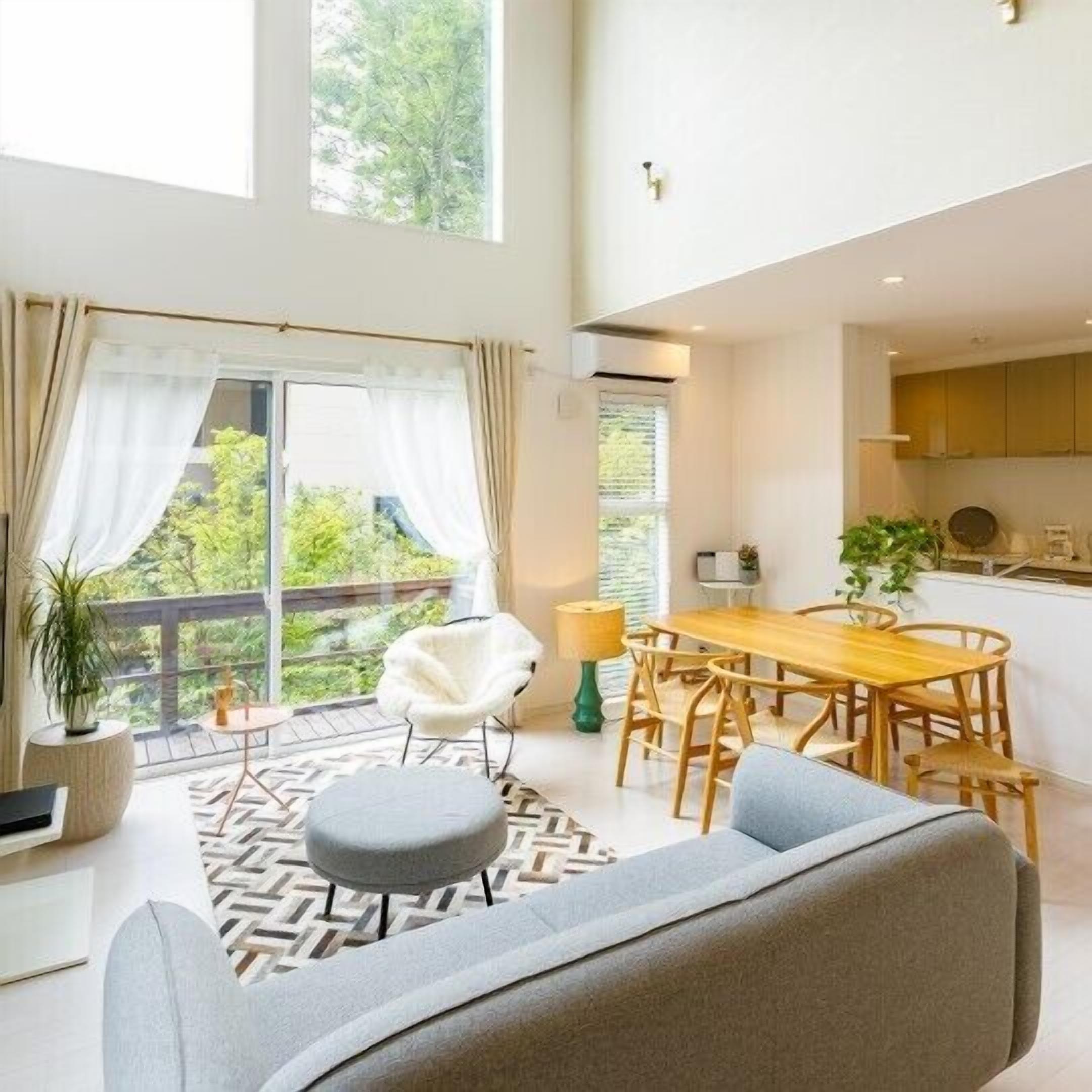 A modern living space with a dining area, a sofa, a chair, and a view of greenery outside.