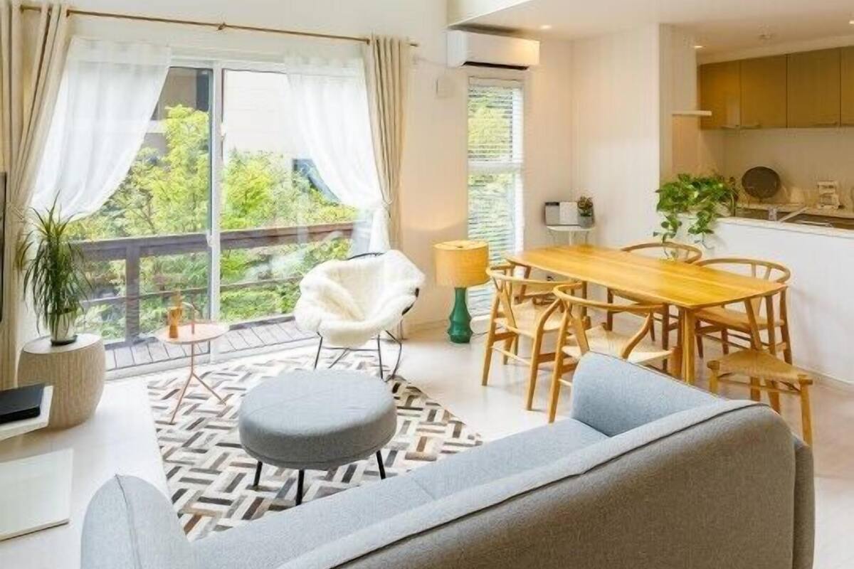 A modern living space with a dining area, a sofa, a chair, and a view of greenery outside.
