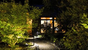 A nighttime view of a building with illuminated windows, surrounded by dense foliage. - Morihaku (Karuizawa)