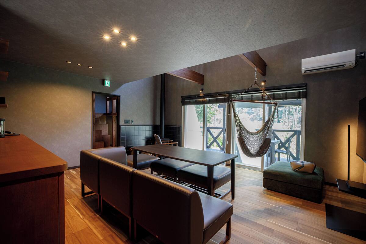 A modern interior with a dining area, seating, a hanging chair, and a large window.