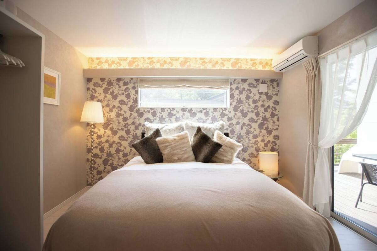 A bedroom with a large bed, floral wallpaper, a window, and an air conditioning unit.