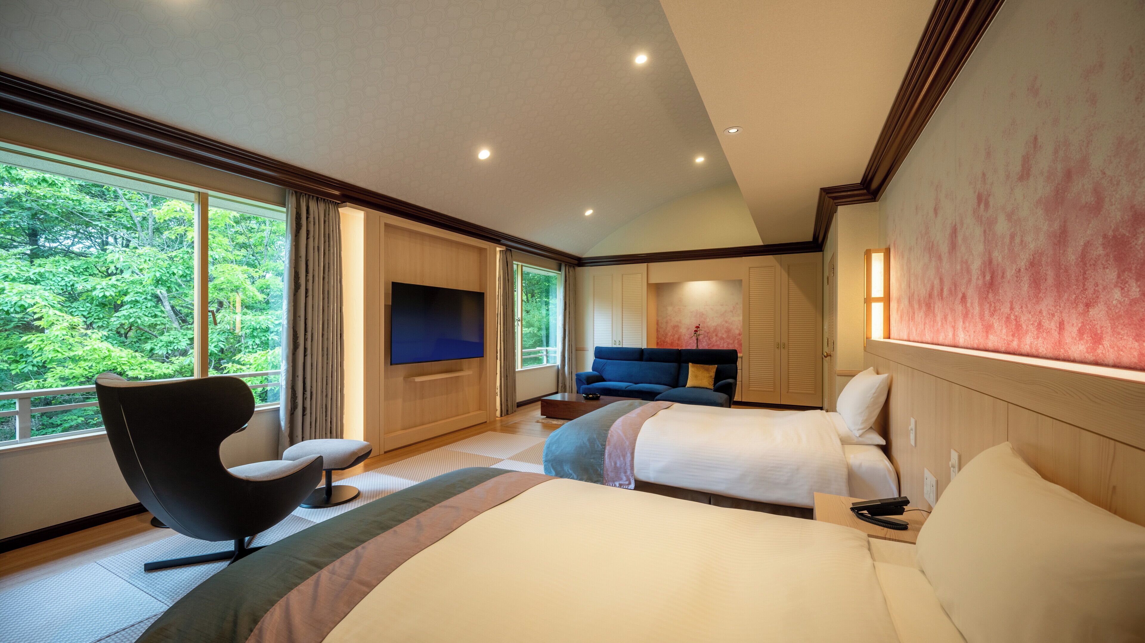 Habitación de hotel con una cama grande, un sofá, un televisor y una ventana con vistas a árboles.