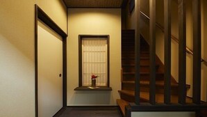Un couloir avec un escalier en bois, une fenêtre avec un rideau et une porte.