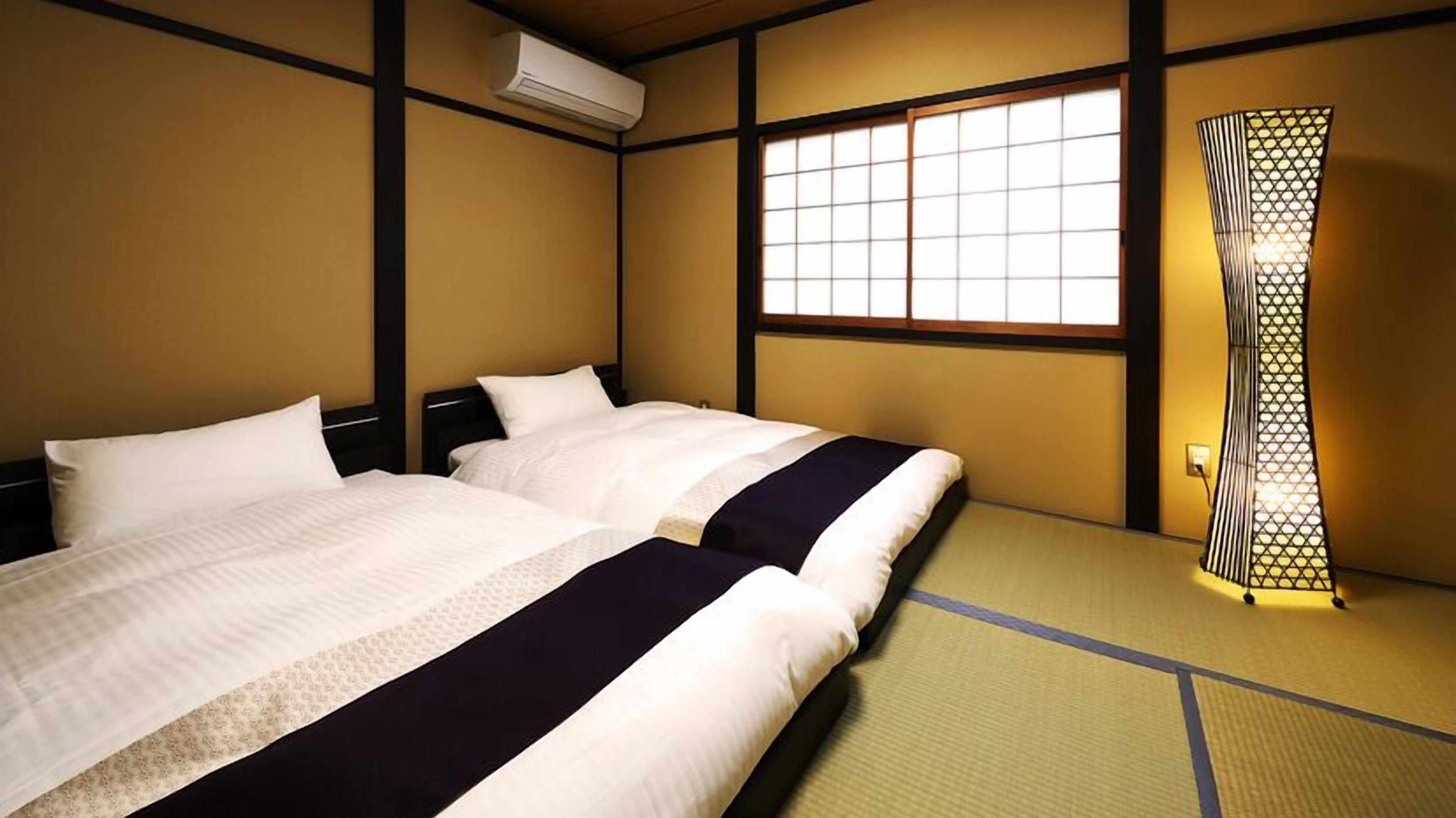 A traditional Japanese-style room with tatami flooring, two beds with white bedding, a sliding door with a geometric pattern, and a window with a grid design.