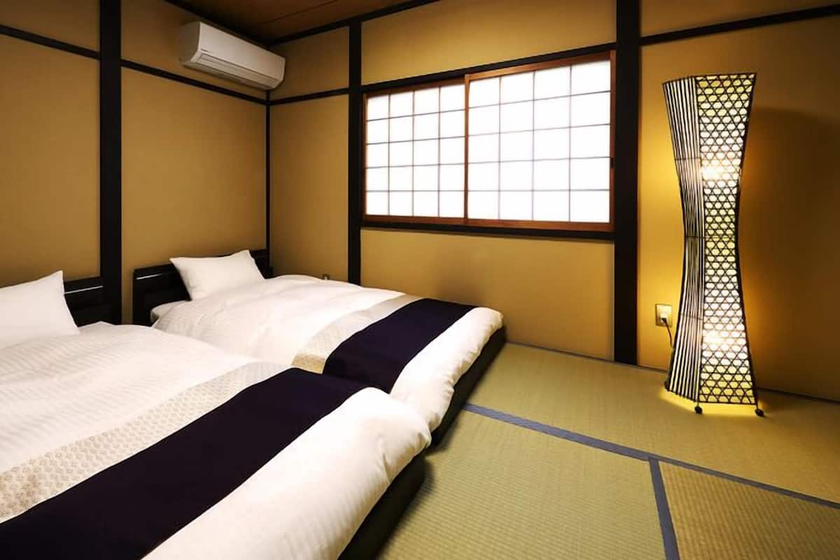 A traditional Japanese-style room with tatami flooring, two beds with white bedding, a sliding door with a geometric pattern, and a window with a grid design.