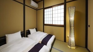 Ein traditioneller japanischer Raum mit Tatami-Böden, einem Bett mit weißer Bettwäsche, einem Fenster mit Gitterstruktur und einem Heizkörper.