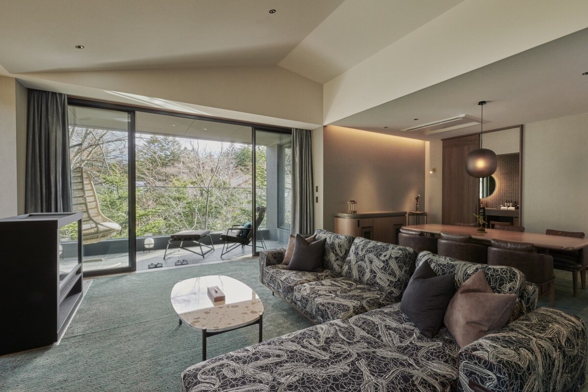 A modern living room with a patterned sofa, a small table, and a dining area with a wooden table and chairs.