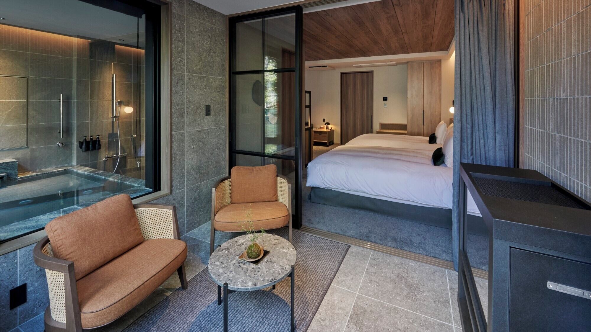 A modern hotel room with a glass-enclosed shower, a sofa, a small table, and a bed.