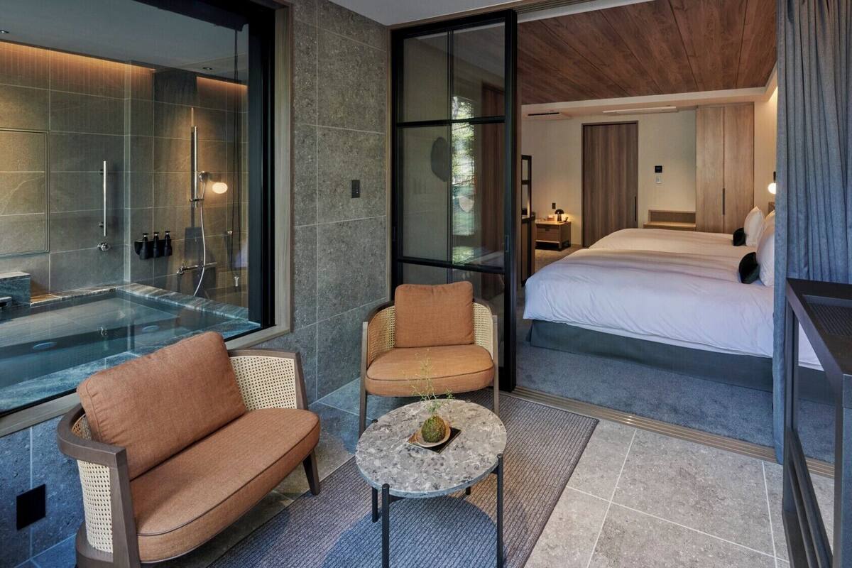 Quarto de hotel moderno com chuveiro em box de vidro, um sofá, uma mesa pequena e uma cama.