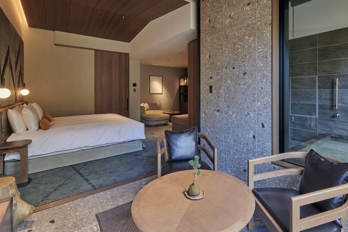 Quarto de hotel moderno com cama, área de estar e vista para uma parede de pedra e um chuveiro de vidro.