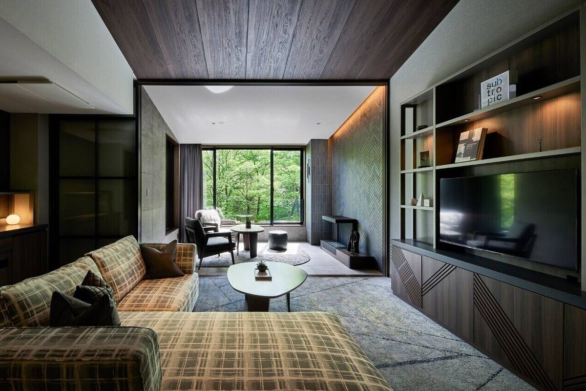 Sala de estar moderna com sofá, mesa de centro e televisão. Há uma janela grande com vista para o verde.