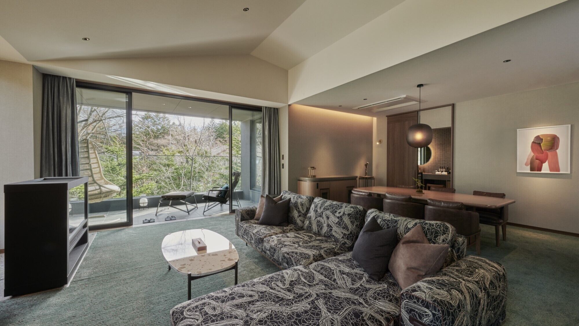 A modern living room with a patterned sofa, a small table, and a dining area with a wooden table and chairs.