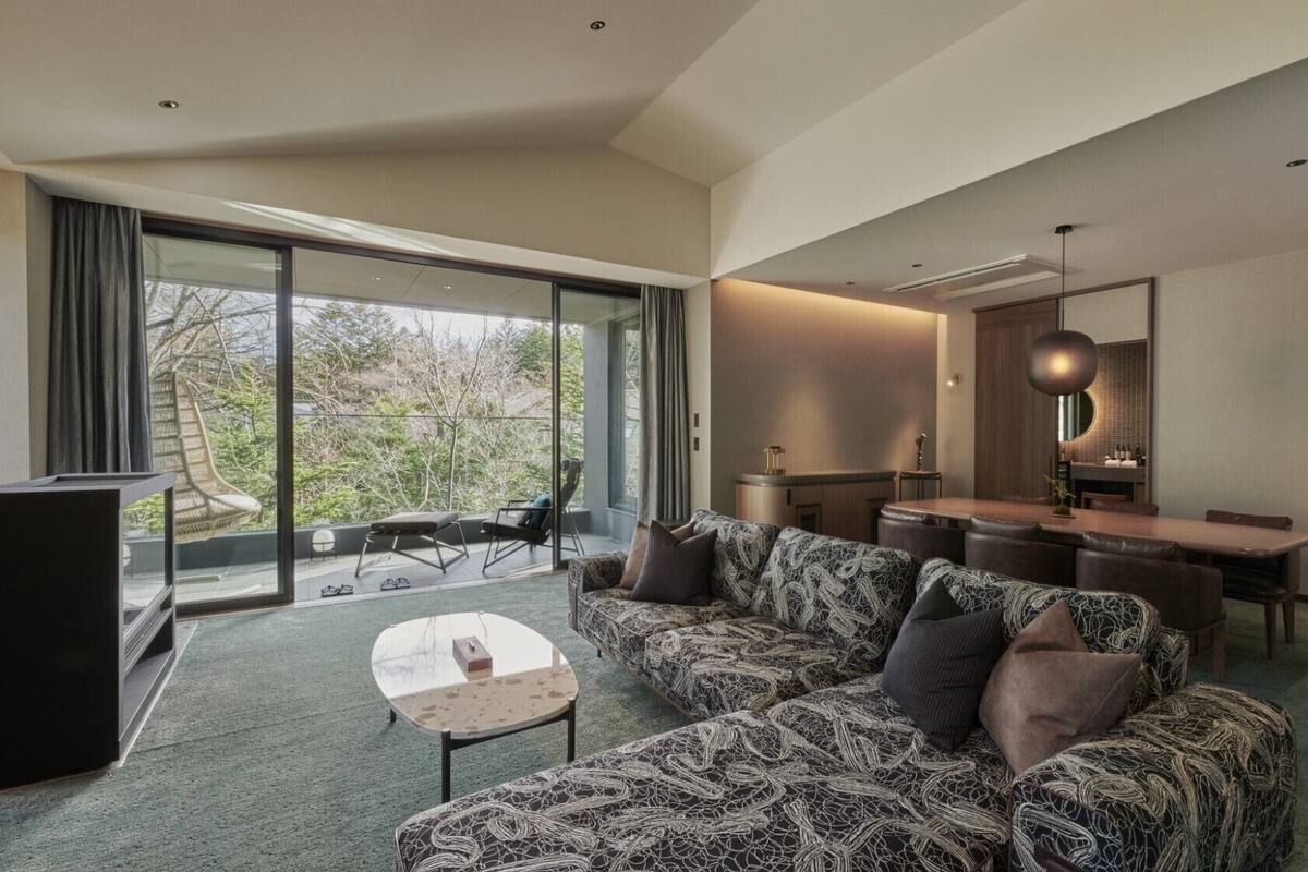 Uma sala de estar moderna com um sofá estampado, uma mesinha e um espaço de refeições com uma mesa e cadeiras de madeira.