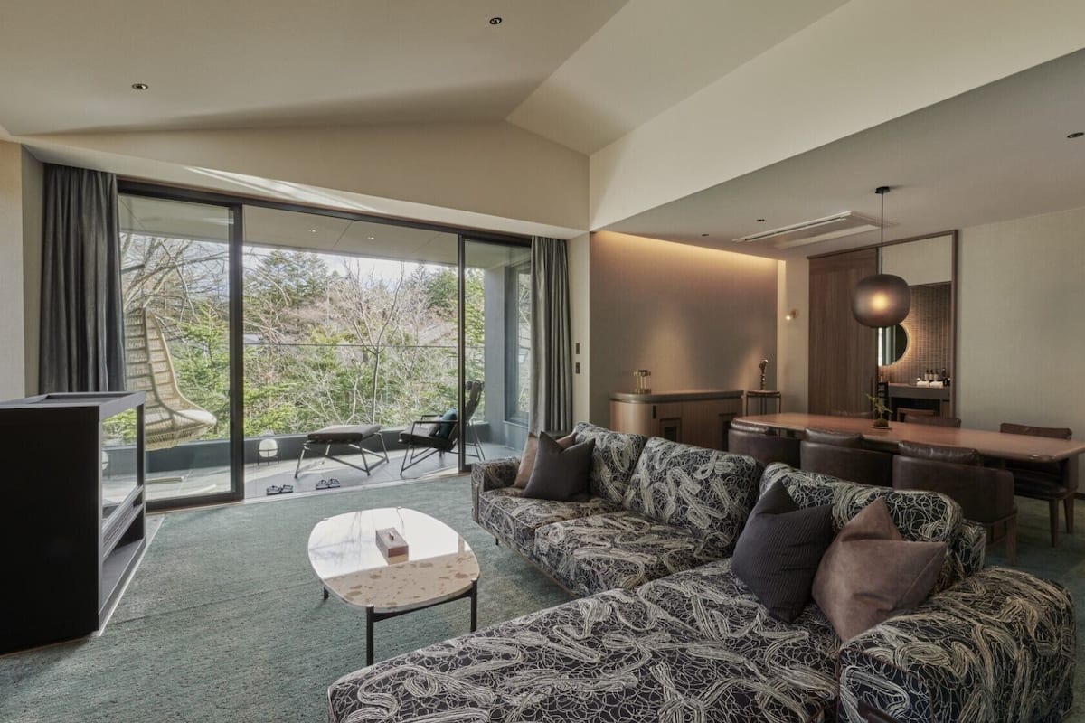 A modern living room with a patterned sofa, a small table, and a dining area with a wooden table and chairs.