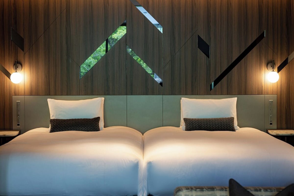 Uma cama de casal com cabeceira, duas mesas de cabeceira e uma parede com padrões geométricos.