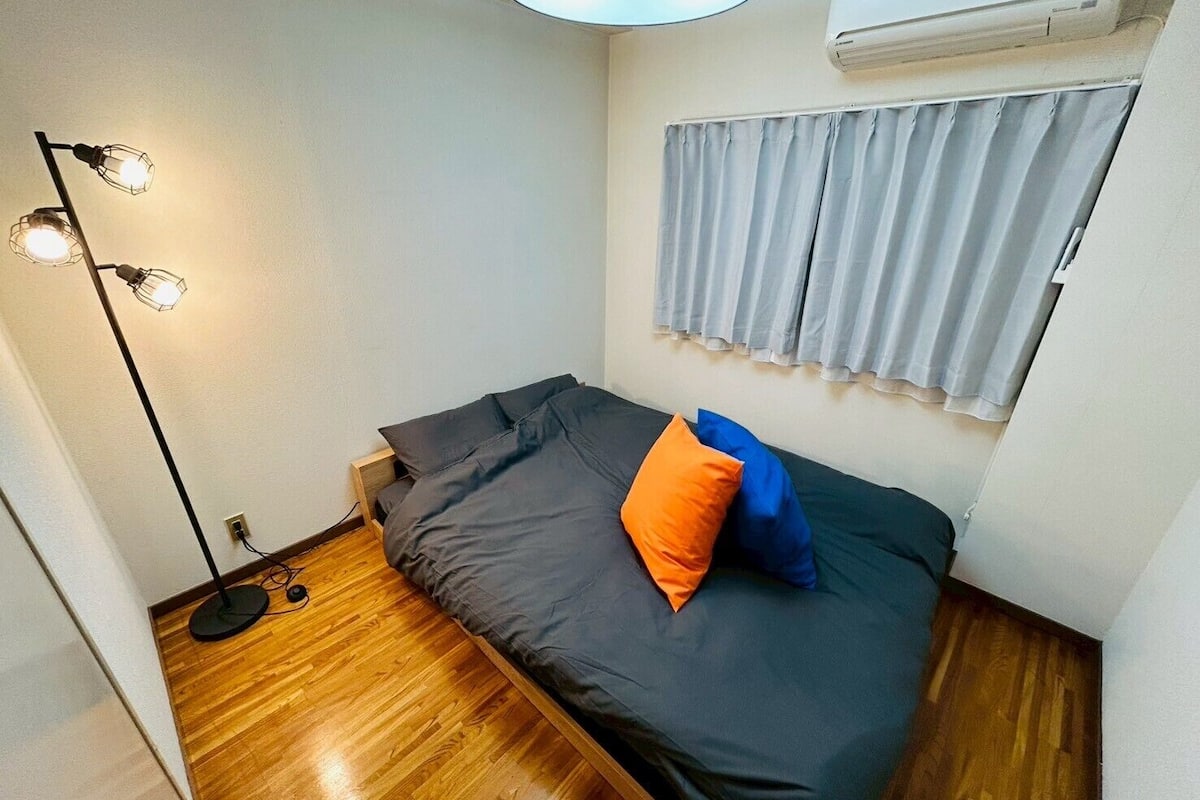 A small, modern bedroom with a bed, a floor lamp, and a window with curtains.