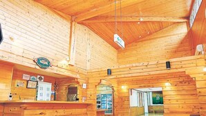 A spacious wooden cabin interior with a reception desk, a fireplace, and a visible door leading to another room. - Yunni no Yu (Yuni)